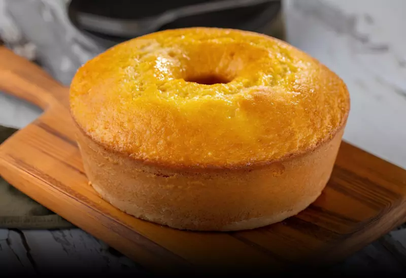 Um bolo de bolo de milho de lata com fubá em cima de uma tábua de carne pronta para ser servida.