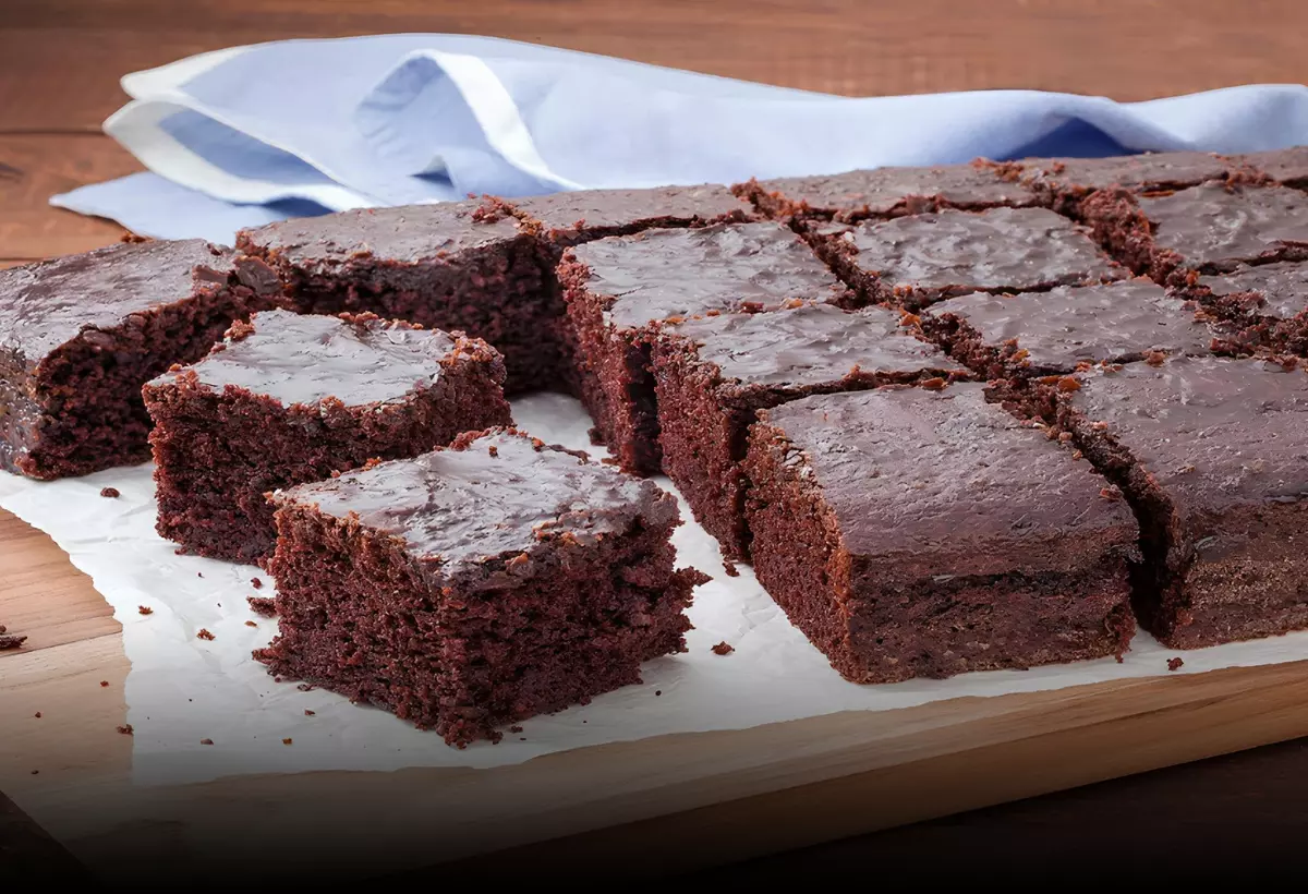 Um bolo de nega maluca tamanho família cortado em vários pedaços em cima de uma tábua para bolo.