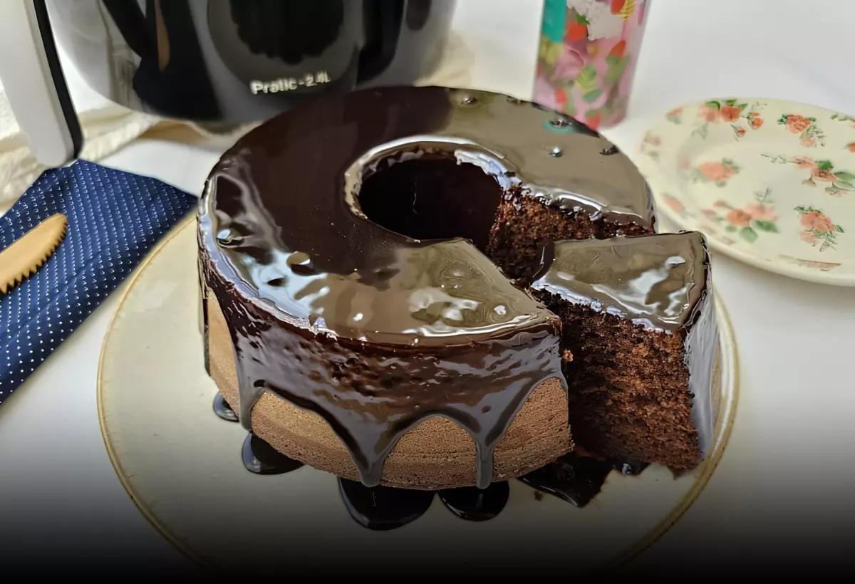 um bolo nega maluca feito na airfryer, com cobertura de chocolate em cima de uma mesa preparada para café da tarde.