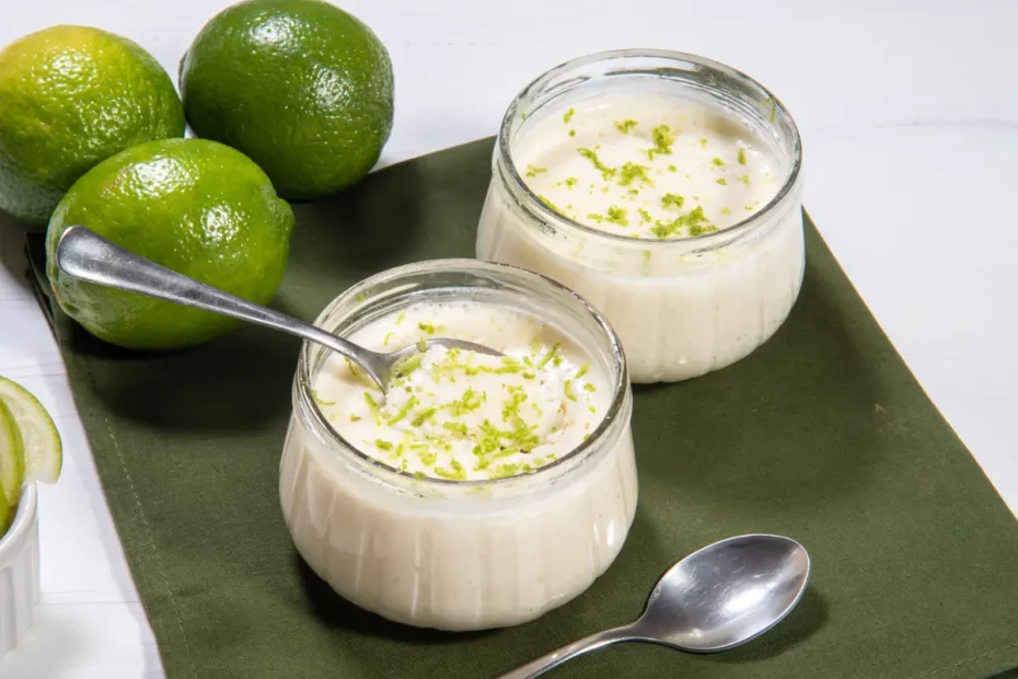 Uma mesa com duas taças com mousse de limão low carb prontos para serem servidos, três limões atrás para decorar.