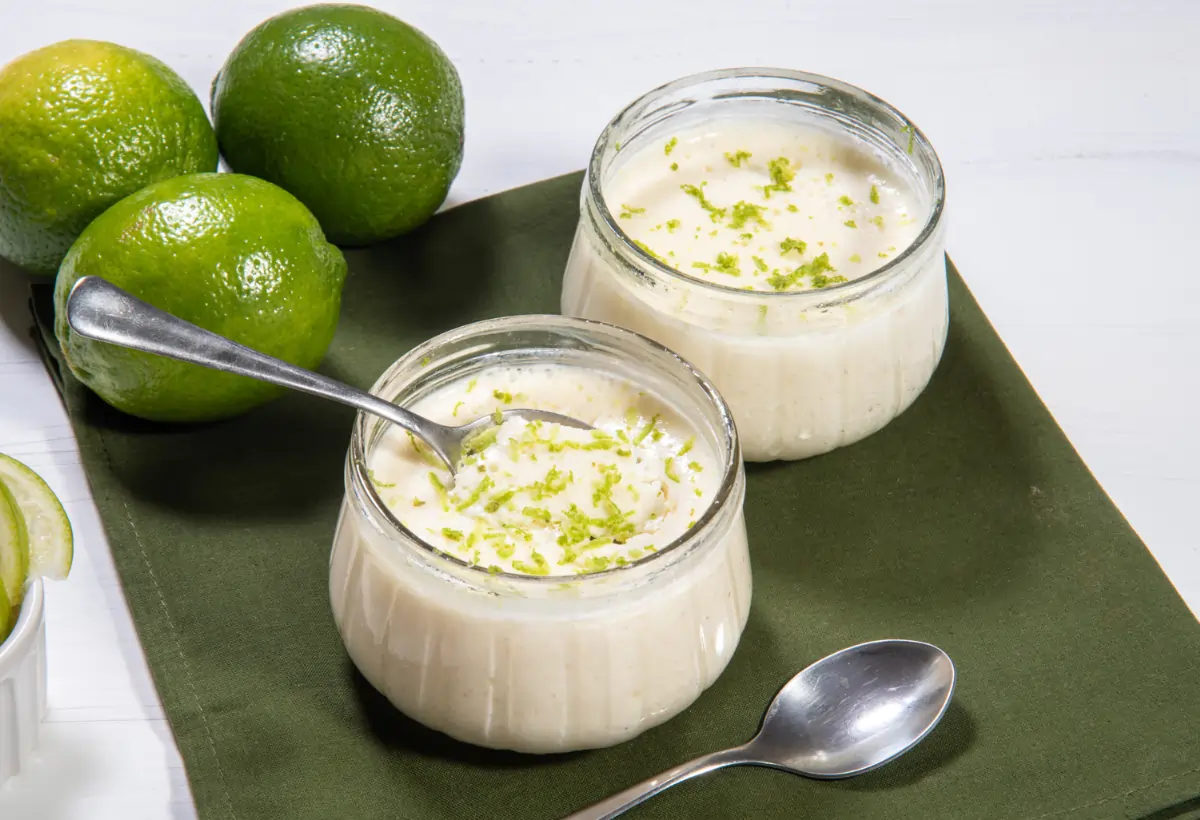 Uma mesa com duas taças com mousse de limão low carb prontos para serem servidos, três limões atrás para decorar.