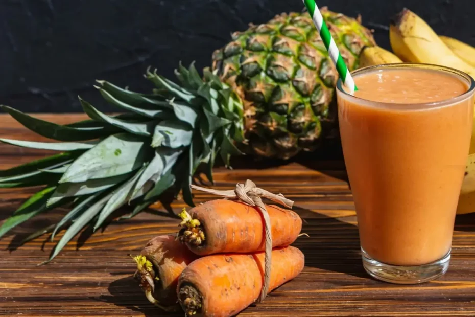 Uma vitamina anti-inflamatória em uma mesa, com um abacaxi e algumas cenouras em cima de uma mesa.