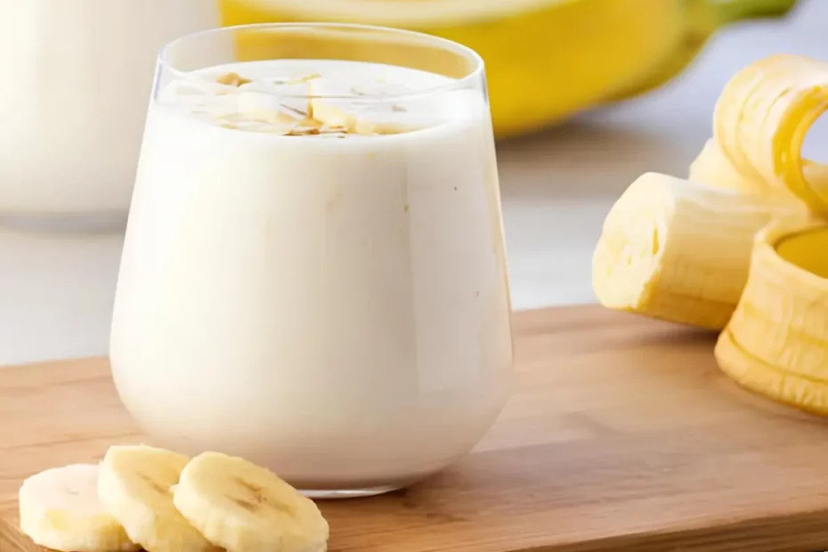 Um copo com uma vitamina de banana cremosa em uma mesa com uma banana picada ao lado para decorar a mesa.