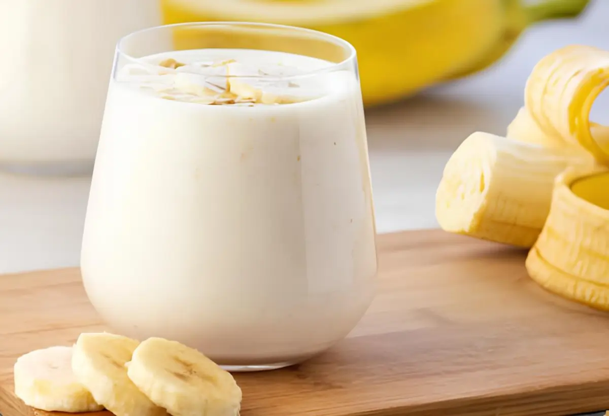 Um copo com uma vitamina de banana cremosa em uma mesa com uma banana picada ao lado para decorar a mesa.