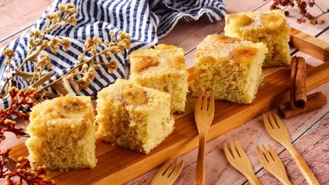 Uma mesa decorada para café da manhã com uma mesinha de madeira com fatias de bolo de banana com flocos de milho.