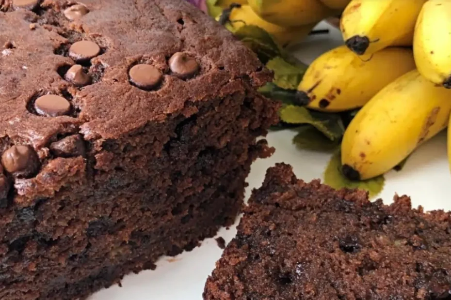 Um bolo de banana com gotas de chocolate com um cacho de bananas em cima da mesa para decorar.