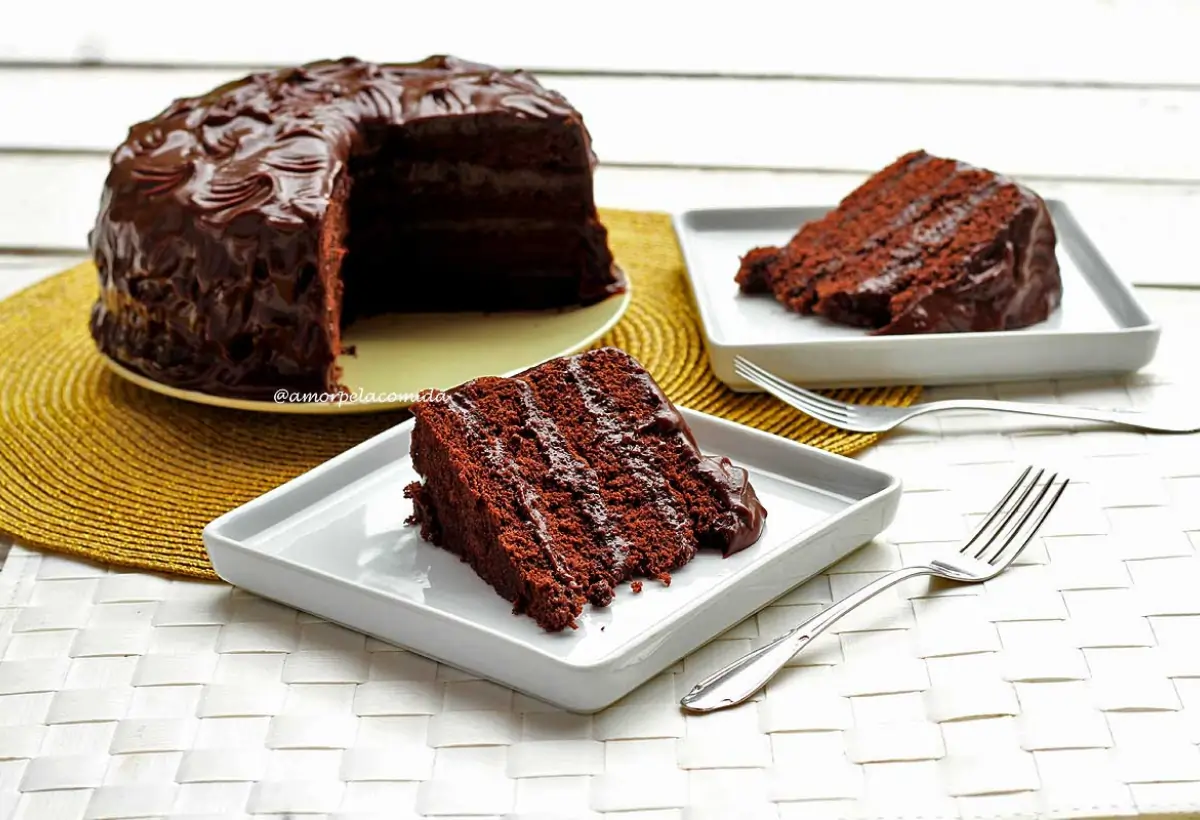 Um bolo de chocolate para aniversário com dois pratos com fatias do bolo para ser servido.