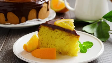 Uma mesa pronta com um bolo de laranja com cobertura de chocolate.