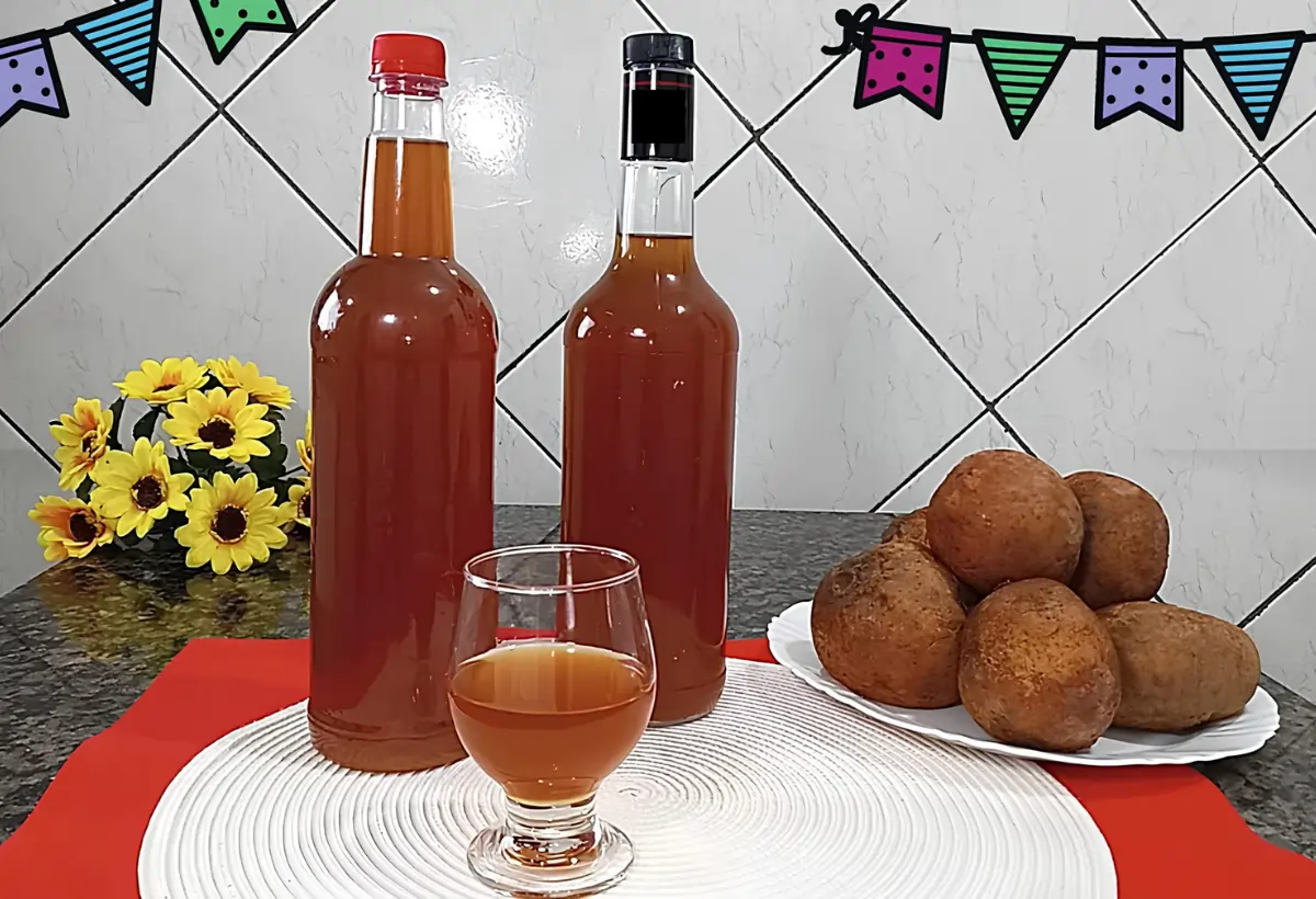 Uma mesa decorada para festa junina com duas garrafas de vidro com um copo de licor de jenipapo com gengibre.