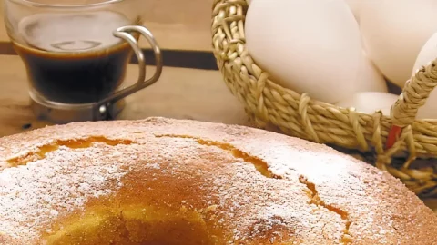 Um bolo de fubá feito sem óleo em uma mesa preparada para o café da tarde.